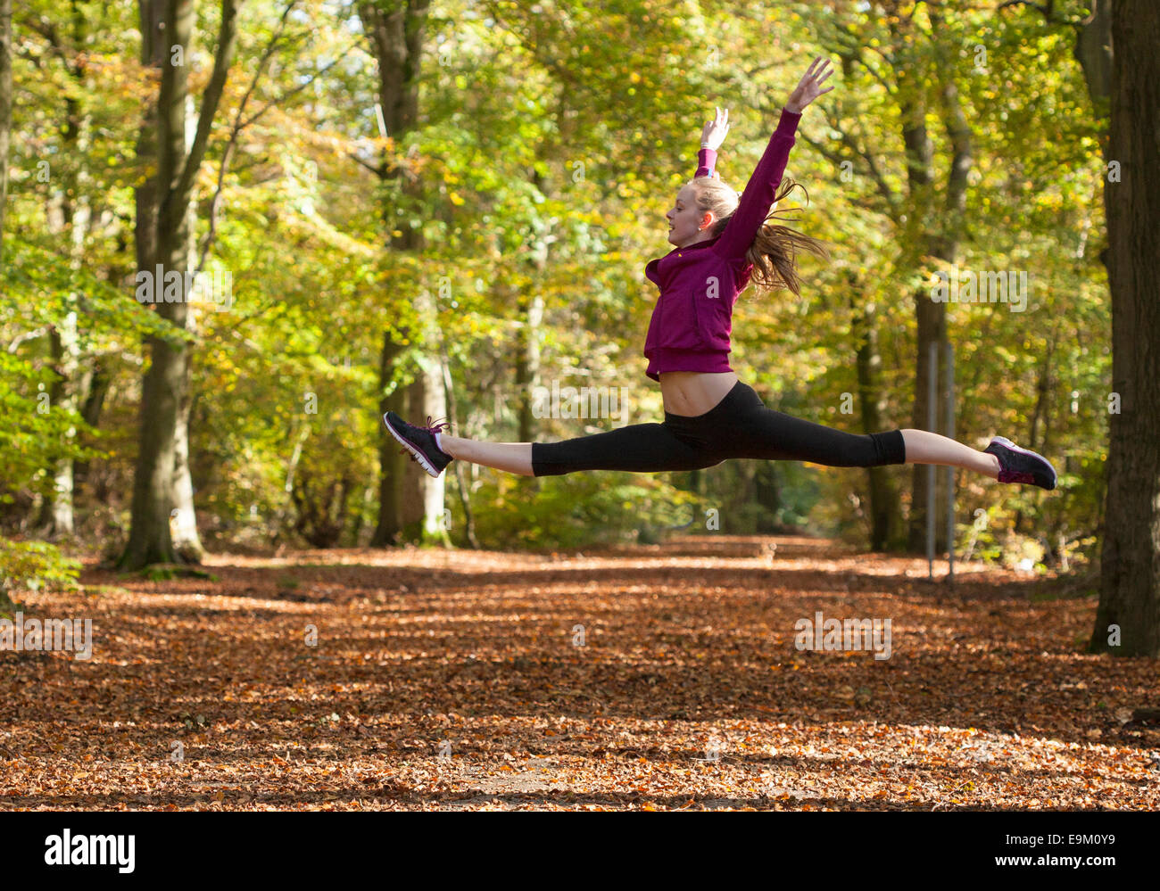 Giovane donna facendo split leap salto in autunno boschi Foto Stock