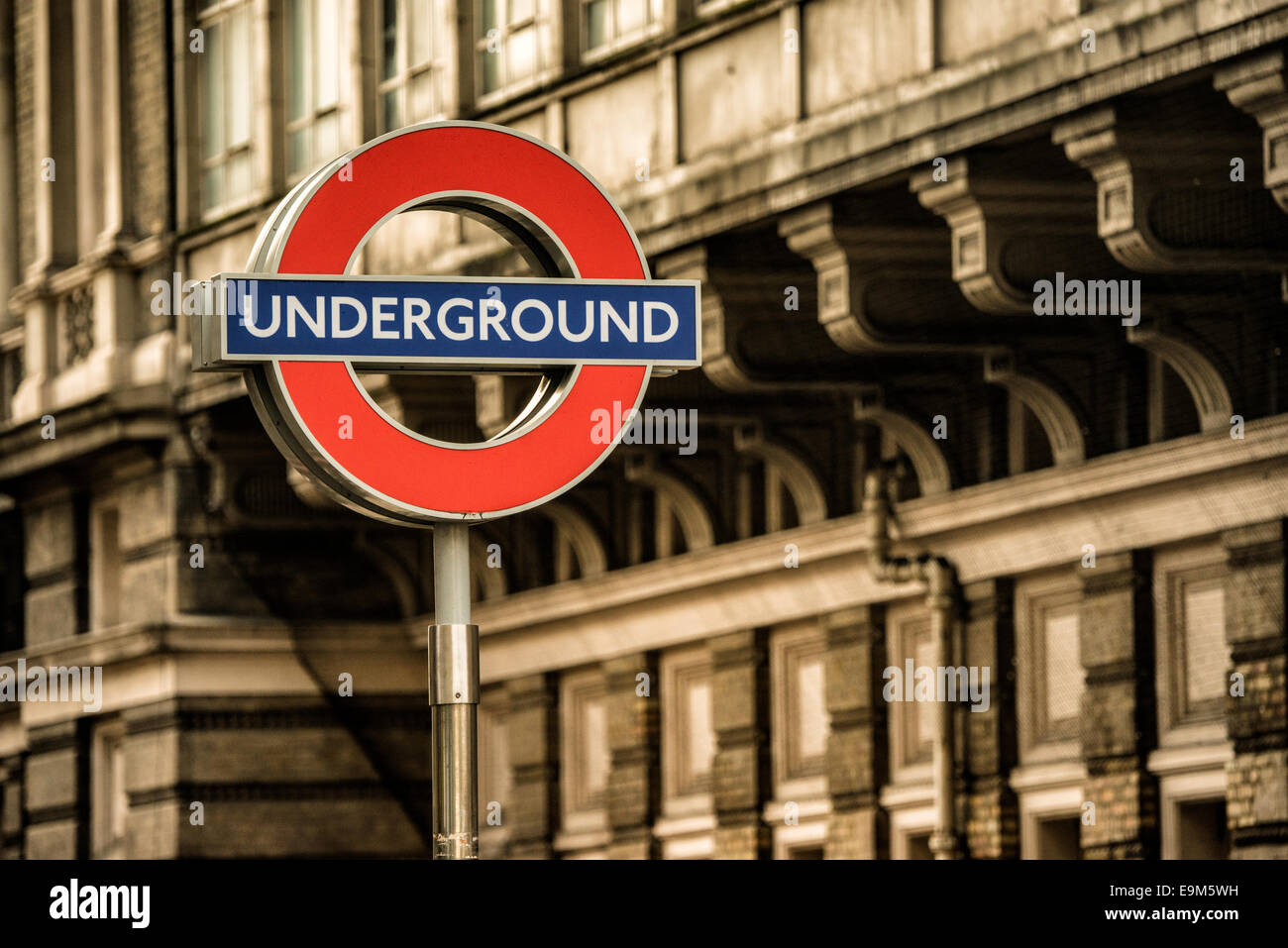 London Underground Sign Roundel London United Kingdom // LONDON, United Kingdom - l'iconico cartello della metropolitana di Londra, con un cerchio rosso e una barra blu, segna l'ingresso a una stazione della metropolitana. Conosciuto come la "rotonda", questo simbolo è un emblema ampiamente riconosciuto del sistema di trasporto pubblico di Londra. La metropolitana di Londra, comunemente nota come metropolitana, è una delle più antiche ed estese reti metropolitane del mondo, avendo aperto la sua prima linea nel 1863. Il caratteristico design rotondo è stato parte dell'identità visiva di Londra dal 1908, evolvendosi dai progetti precedenti per diventare il Foto Stock