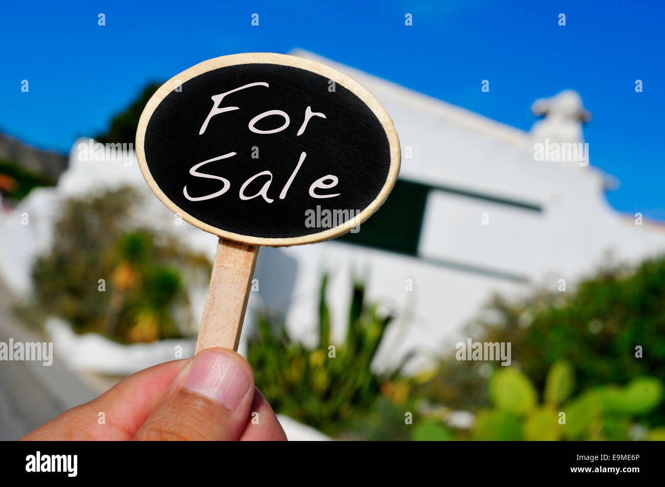 Un man mano che tiene un cartello con scritto il testo per la vendita scritto in esso nella facciata di una casa Foto Stock