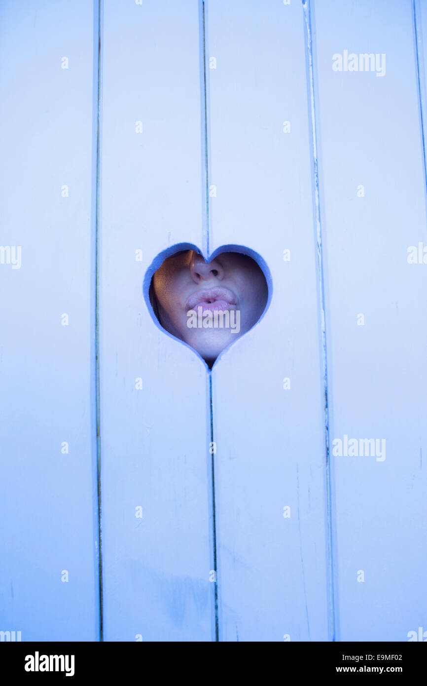 Close-up di donna raggrinzamenti labbra attraverso il cuore di legno di forma Foto Stock