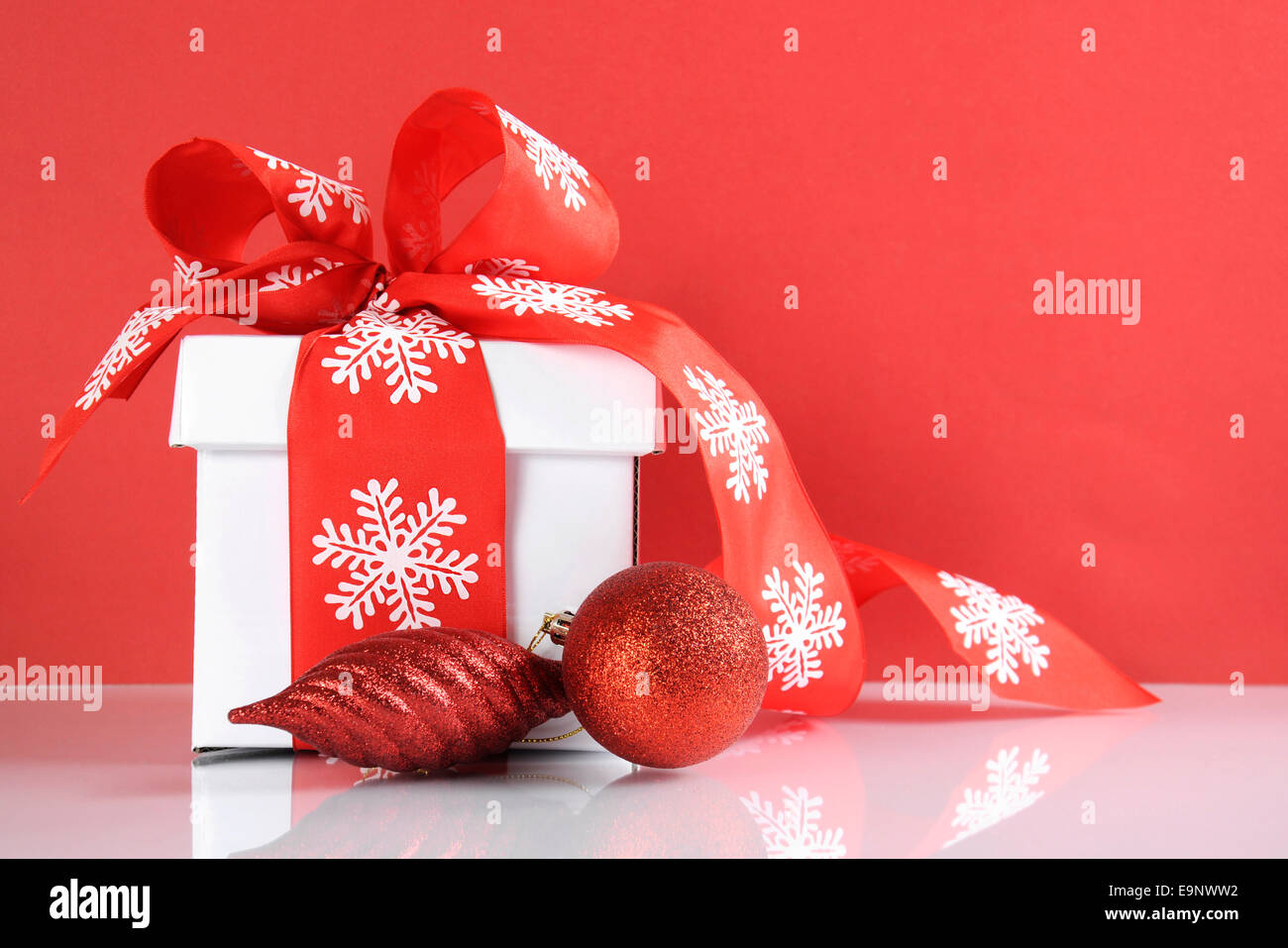 Festive rosso e bianco tema natale scatola regalo su bianco riflettente tabella contro uno sfondo di colore rosso. Foto Stock