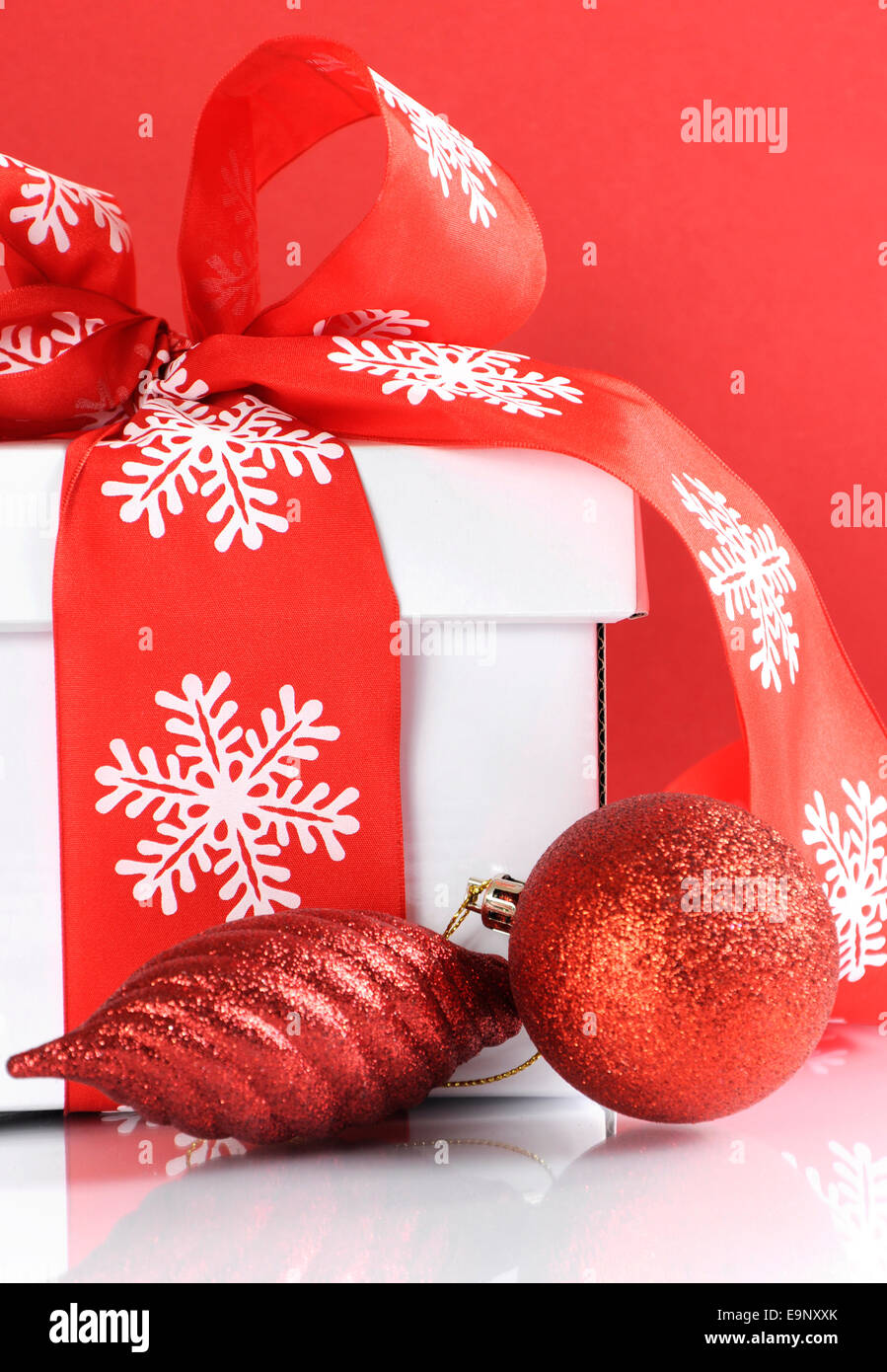 Festive rosso e bianco tema natale scatola regalo su bianco riflettente tabella contro uno sfondo di colore rosso. Close up. Foto Stock