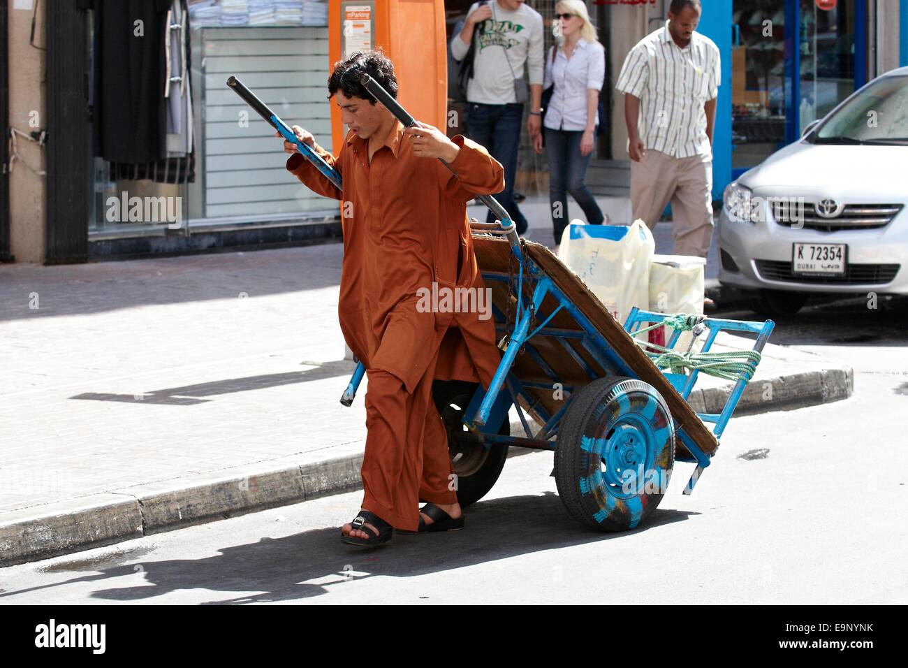 Ragazzo o giovane uomo tirando vuoto carro del mercato vicino il vecchio souk di Dubai City Foto Stock