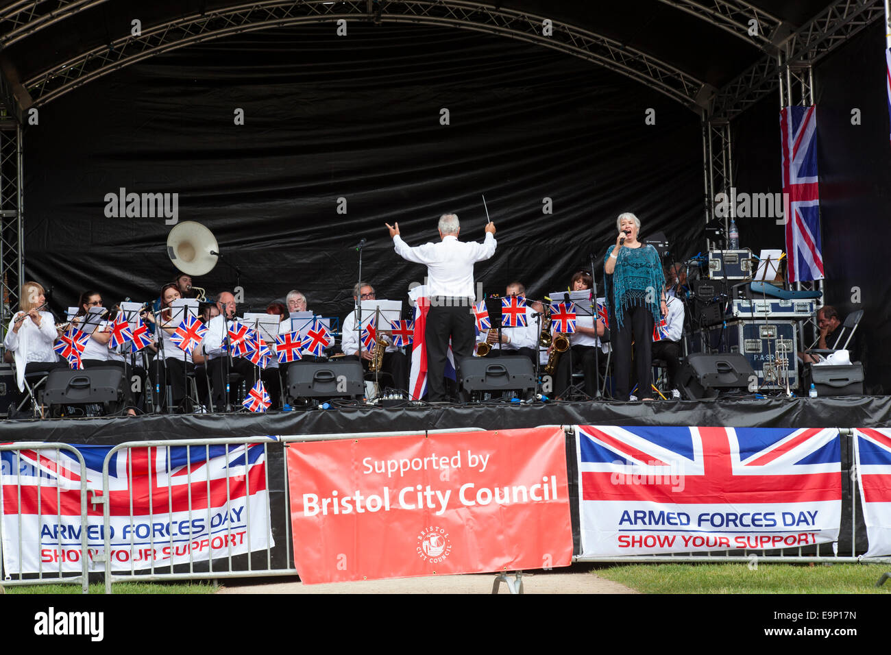 Un conduttore si trova di fronte la fascia mentre una donna cantante esegue sul palcoscenico open-air come parte di "Forze Armate giorno". Foto Stock