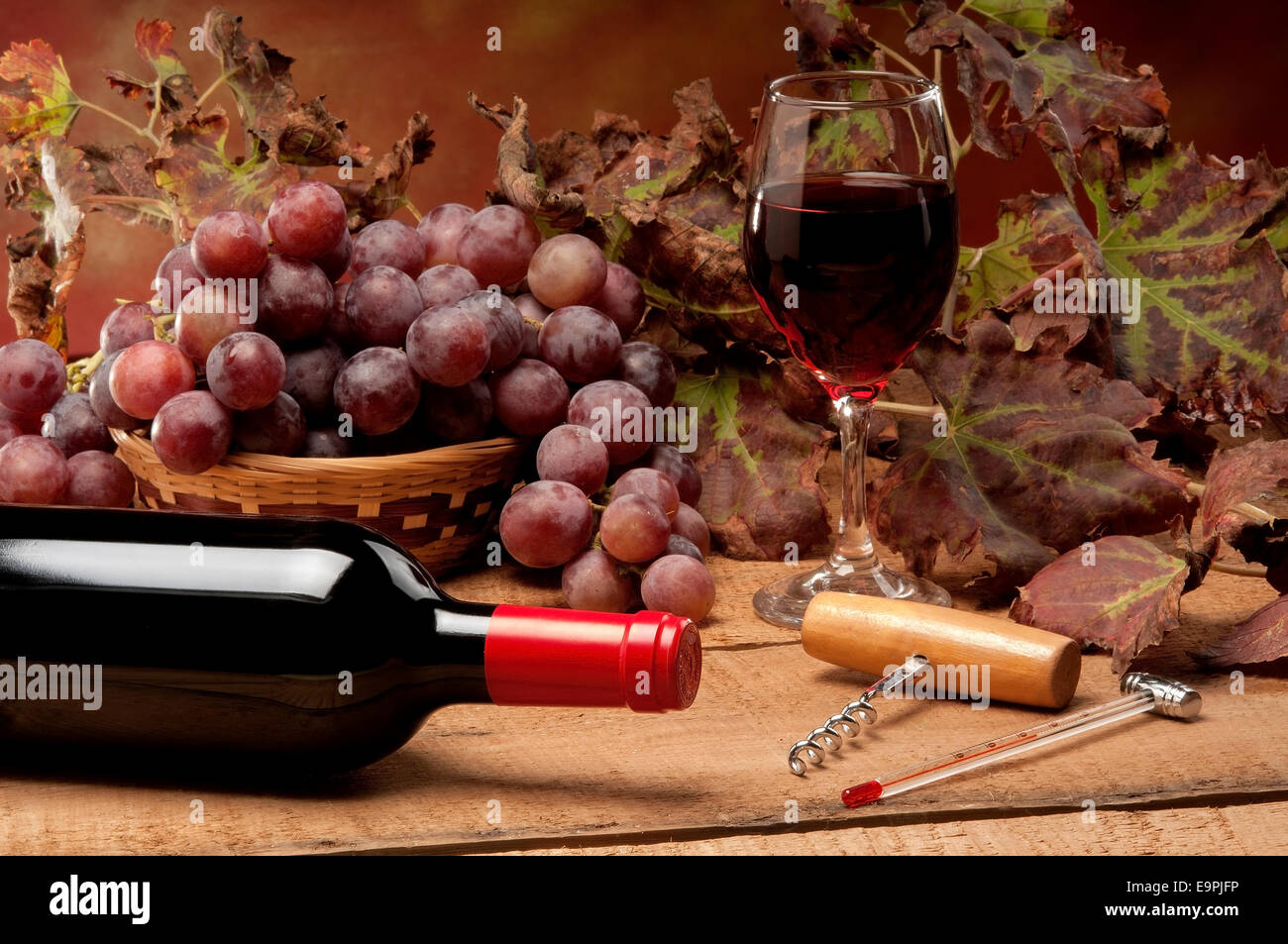 Un vecchio tavolo con una bottiglia di vino, foglie di vite e uva rossa Foto Stock