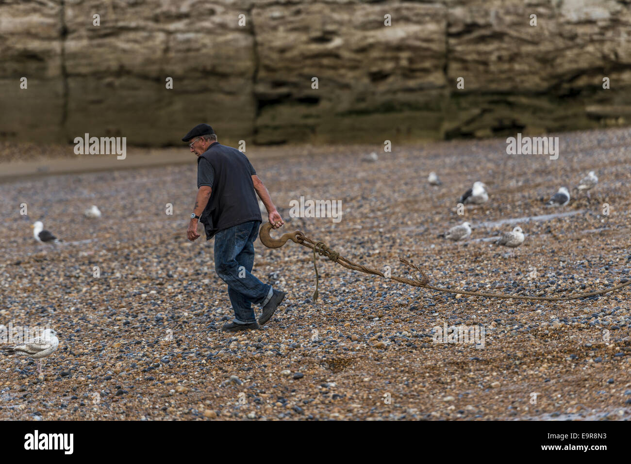 Un lavoratore contribuisce a lanciare la flotta costiera di barche da pesca dalla spiaggia di Stade in Hastings Foto Stock