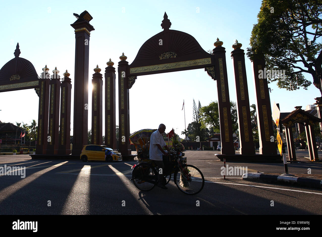 Un riscio' ciclista passa di fronte al cancello che è il punto di riferimento in Kota Bharu, Kelantan. Foto Stock