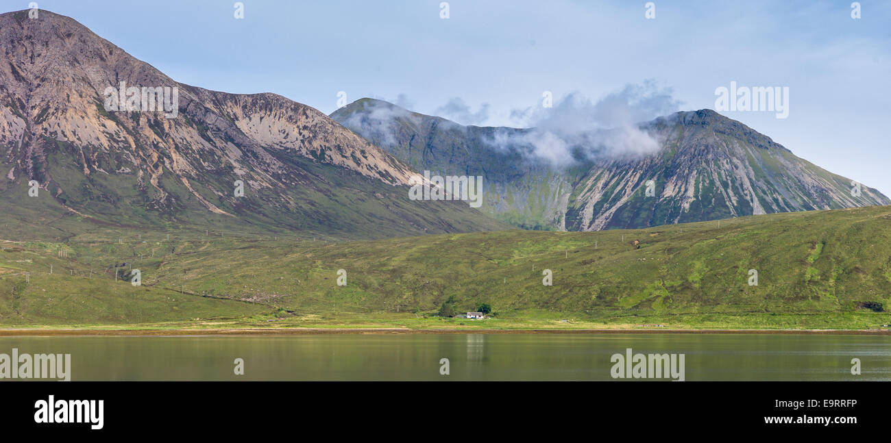 Di piccole dimensioni e di colore bianco crofters solitario cottage immerso sotto la gamma della montagna si riflette nelle acque del loch sull isola di Skye nel Highl Foto Stock