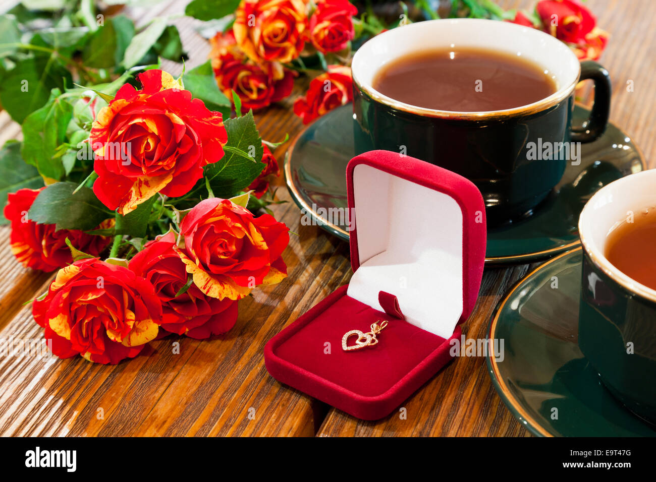 Gioielli in oro in velluto rosso scatola, tazze di tè e bouquet di rose sul tavolo di legno Foto Stock
