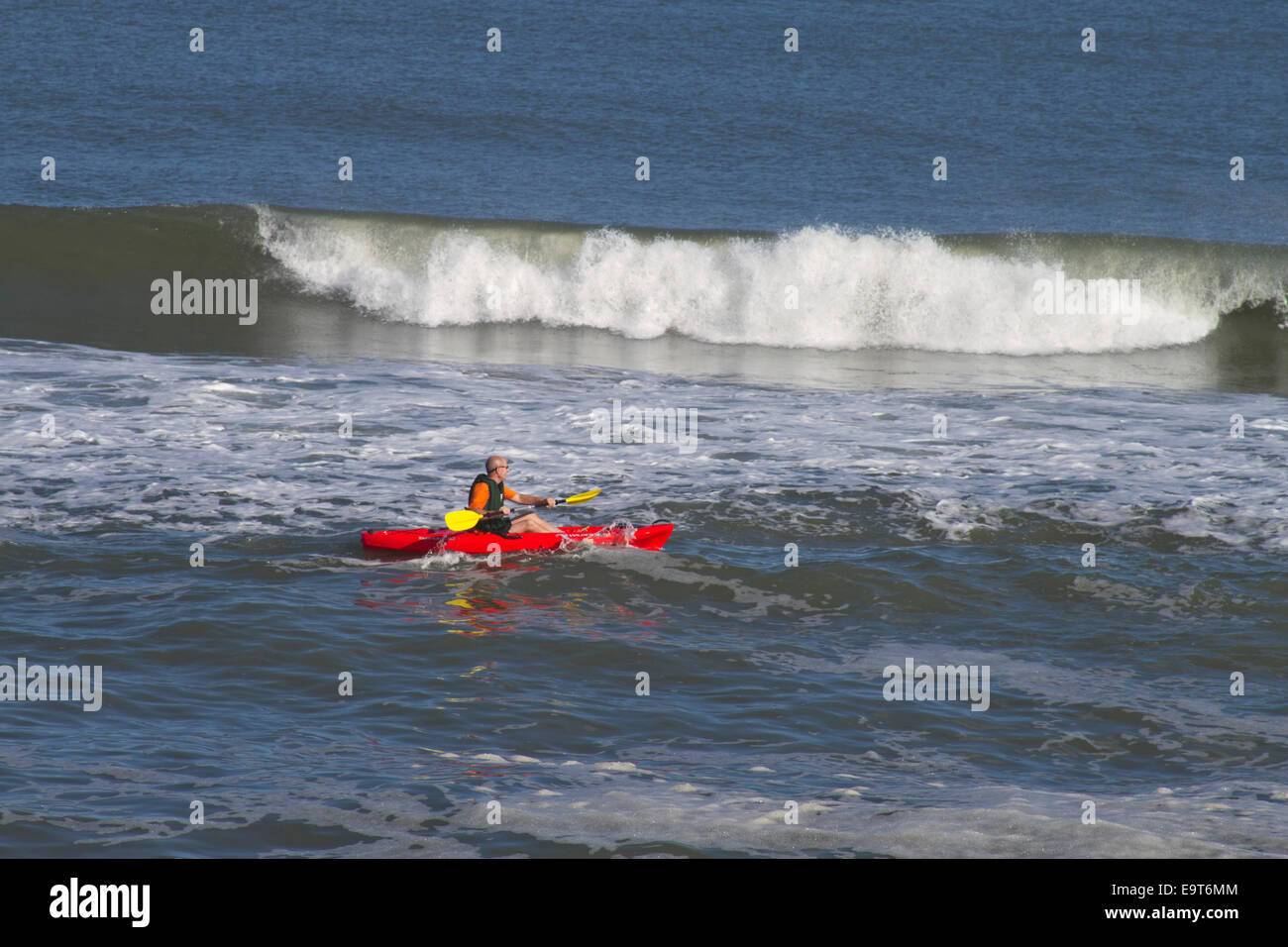 Cape Hatteras, Outer Banks, NC, Stati Uniti d'America - 17 ottobre 2013: un uomo in un colore rosso brillante kayak pagaie al fianco di alte onde del mare Foto Stock
