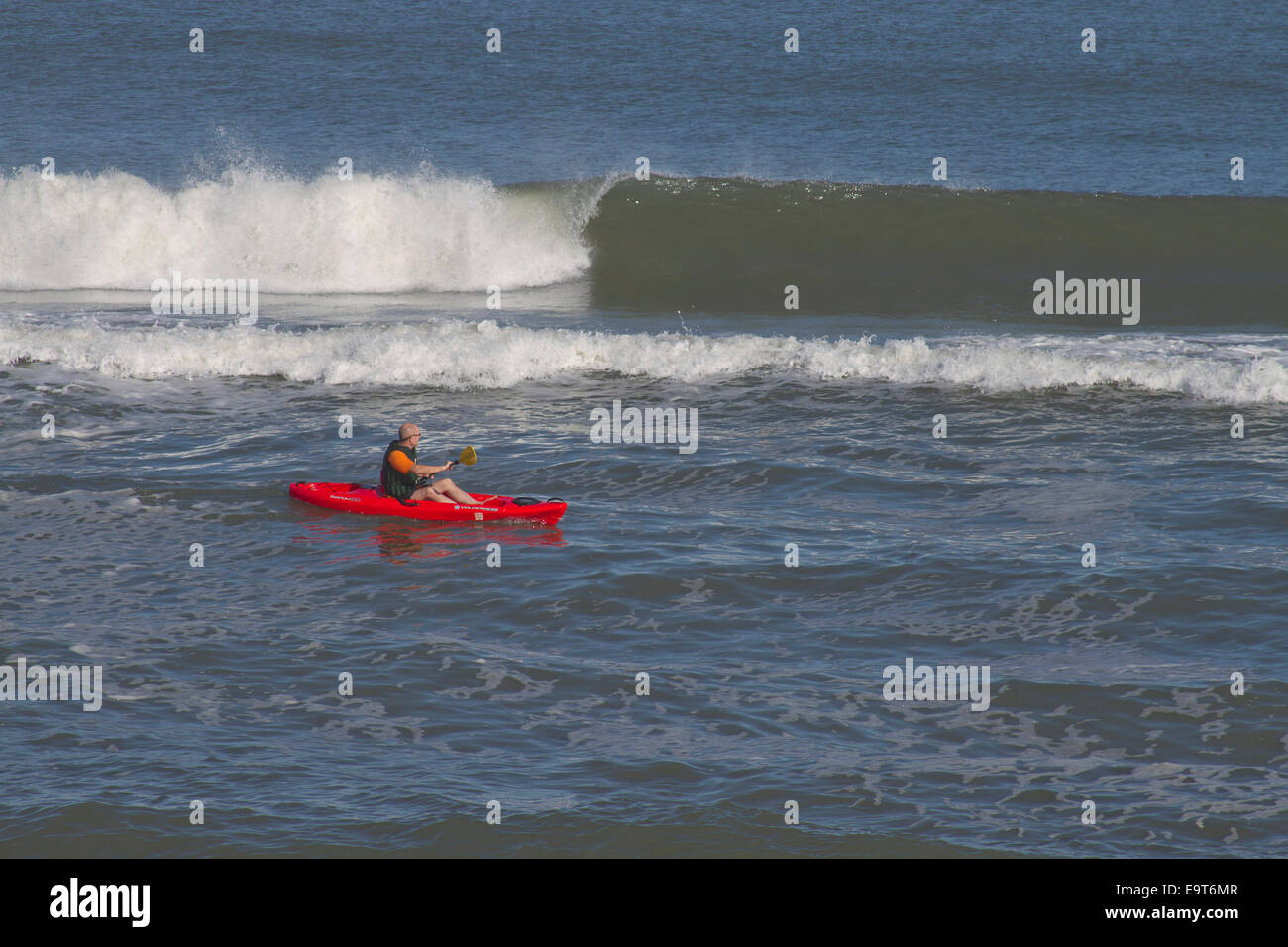 Cape Hatteras, Outer Banks, NC, Stati Uniti d'America - 17 ottobre 2013: un uomo in un colore rosso brillante kayak pagaie al fianco di alte onde del mare Foto Stock