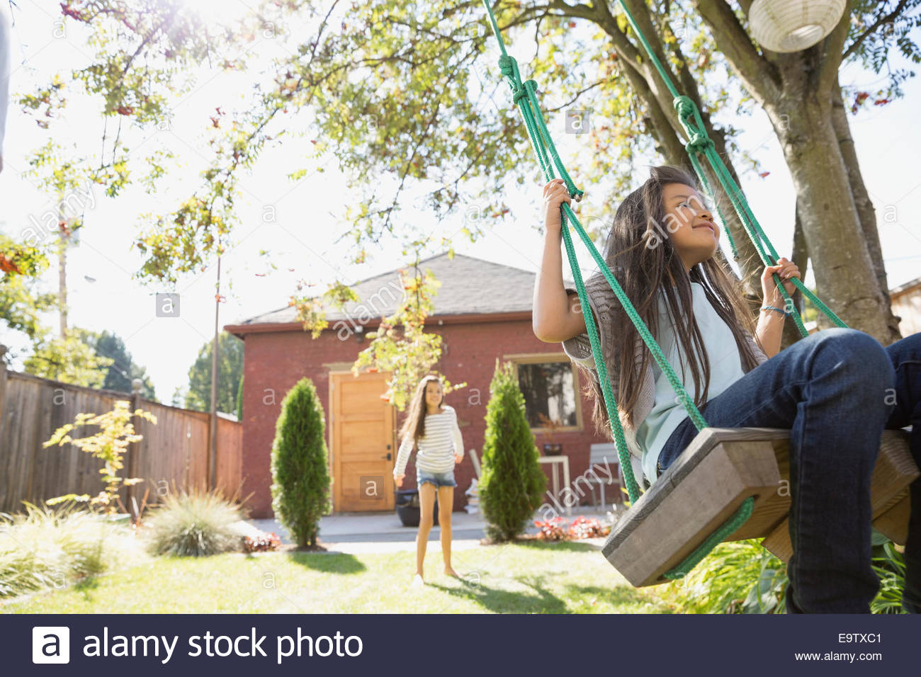 Ragazza su albero oscillante nel cortile soleggiato Foto Stock