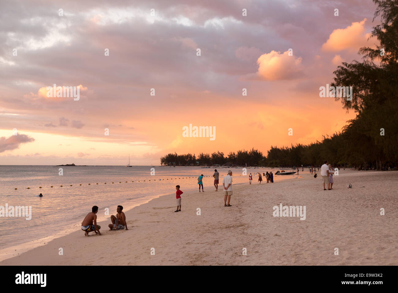 La popolazione locale e i turisti a piedi su una spiaggia tropicale al tramonto; Trou aux Biches Mont Choisy beach, a nord di Mauritius Foto Stock