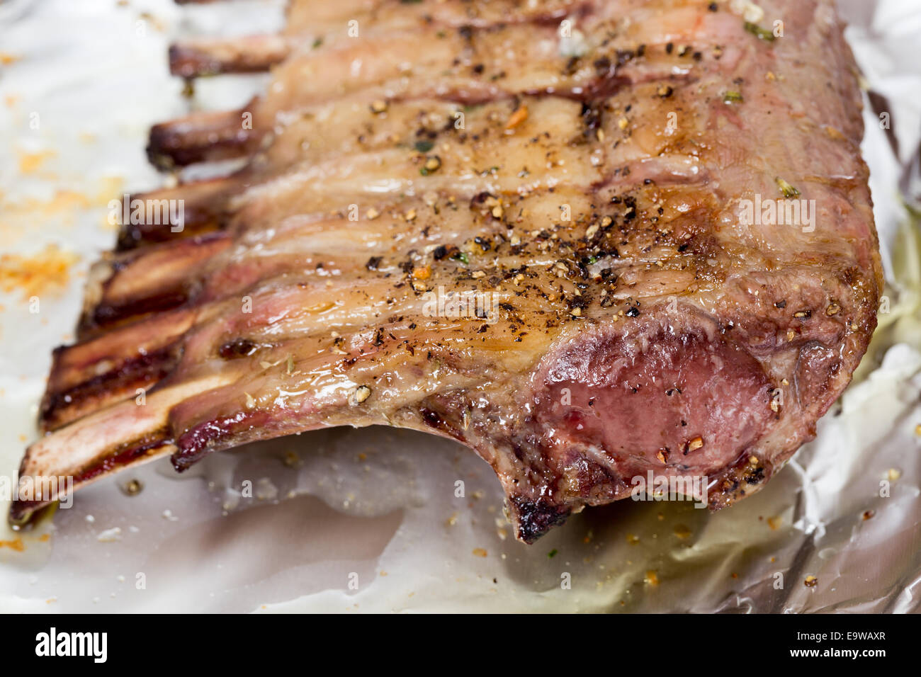 Un carré di agnello sfregata con pepe, sale e aglio, su carta stagnola dopo la torrefazione. Foto Stock