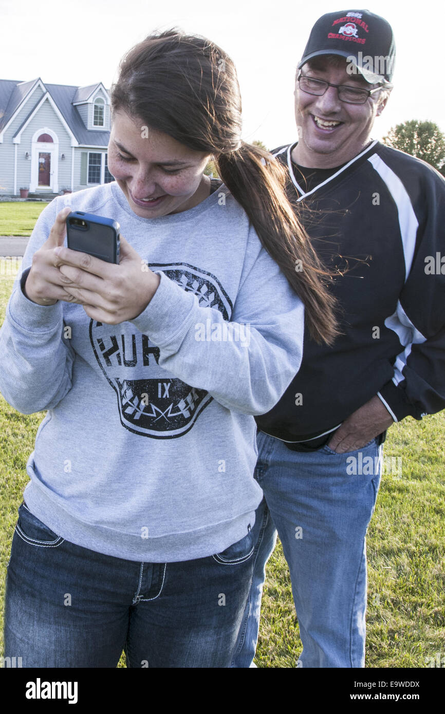 20-30's donna è in piedi fuori gli sms sul suo telefono cellulare. Il suo padre è guardando sopra la sua spalla. Foto Stock