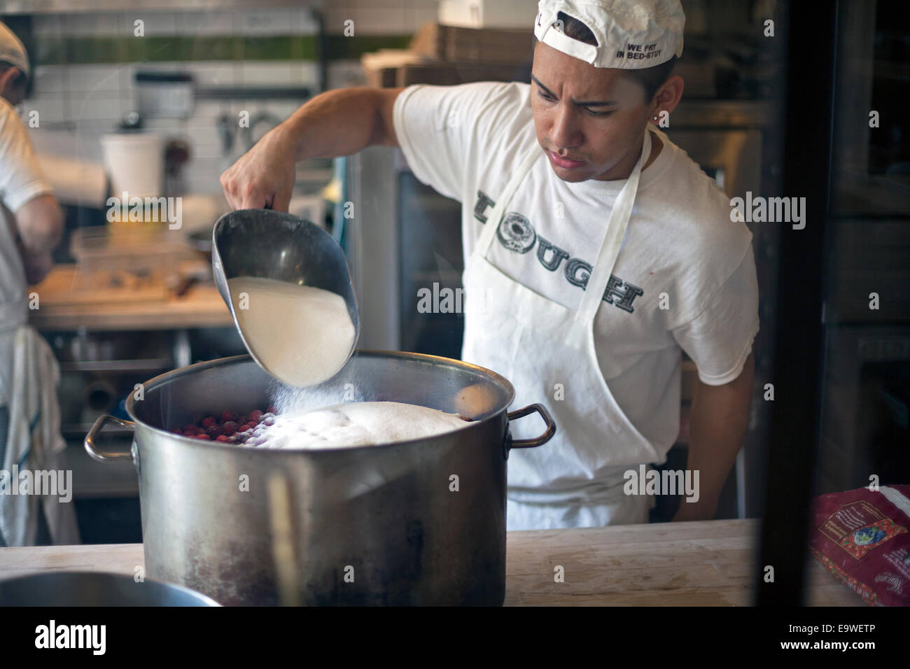Un lavoratore a impasto in Brooklyn aggiunge lo zucchero in una pentola. Foto Stock