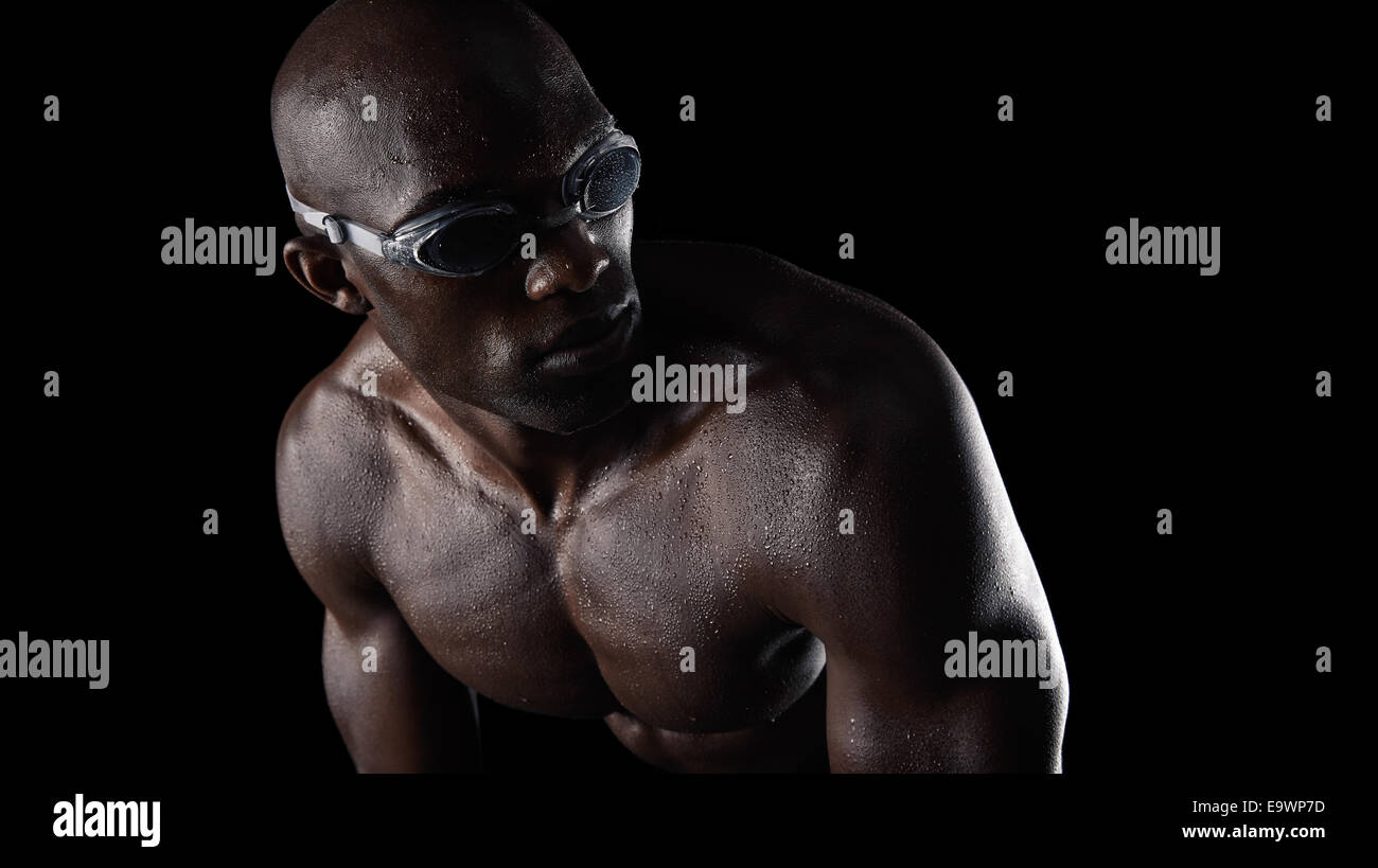 Studio shot del maschio africano nuotatore indossando occhiali guardando sopra la spalla su sfondo nero. Muscoloso giovane atleta. Foto Stock