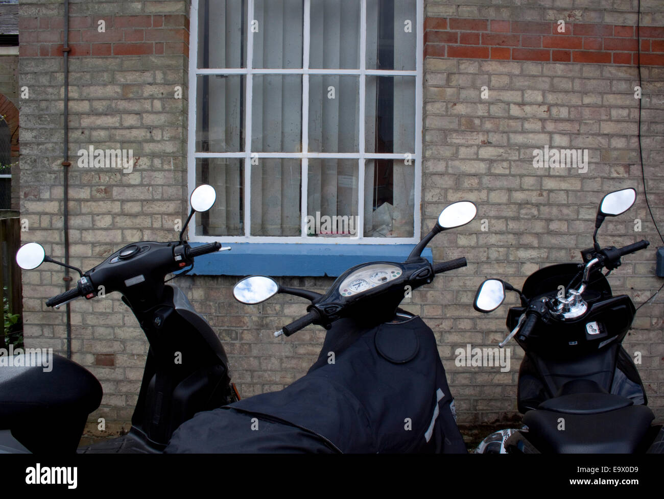 Vista posteriore di tre scooters parcheggiata da un Grigio Grigio muro di mattoni con scooter' specchi riflette il cielo. Foto Stock