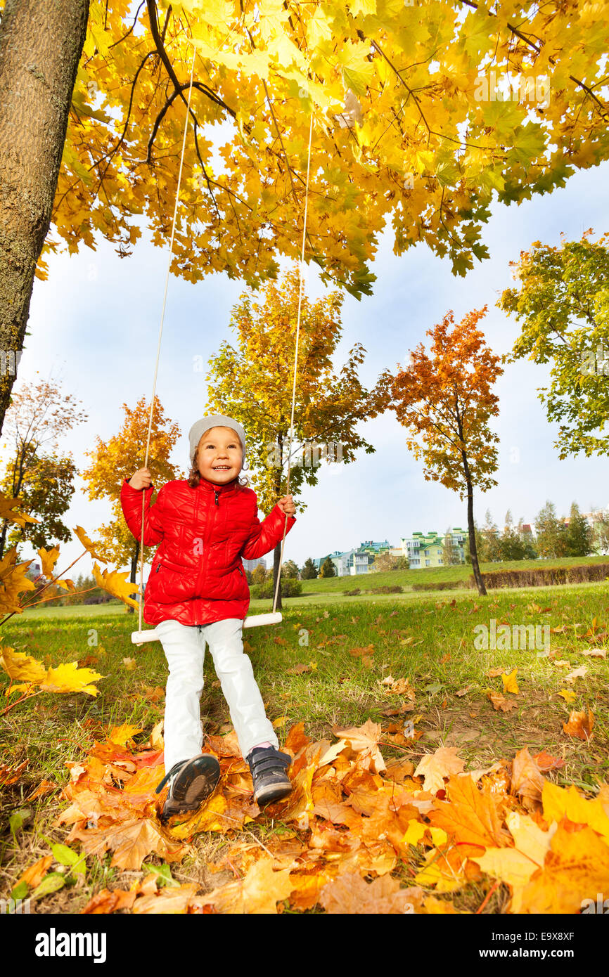 Felice ragazza siede su altalene sorridente durante l'autunno Foto Stock