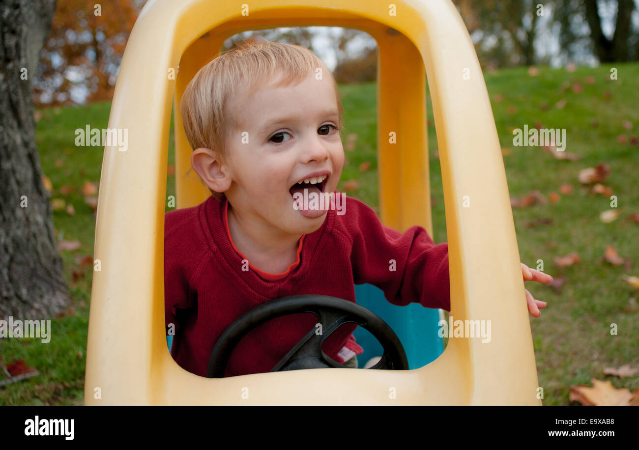 Un bambino fa una faccia felice mentre giocando nel suo giocattolo auto in autunno. Foto Stock