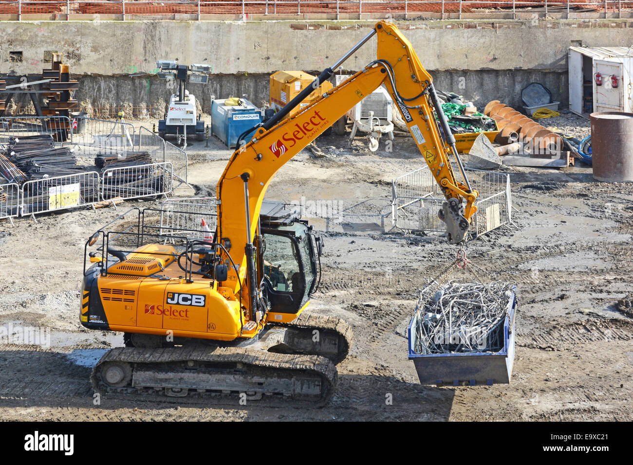 JCB escavatore digger portando il riciclo saltare di barre di acciaio attraverso seminterrato sito in costruzione Foto Stock