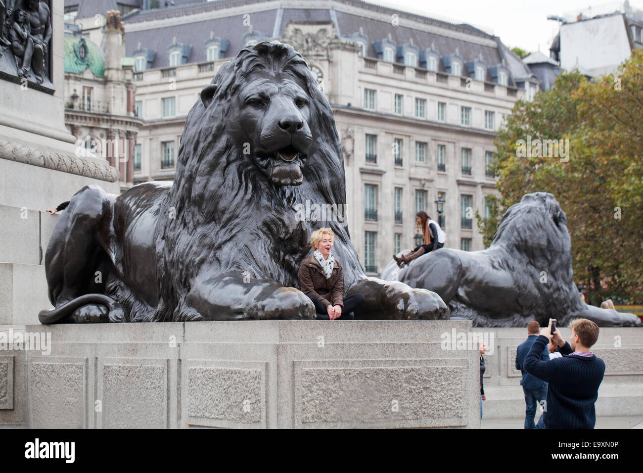 Trafalgar Square. Londra. In Inghilterra. Un 'Landseer Lion' sul plinto in primo piano con la giovane donna in posa per l uomo a fotografare. Foto Stock