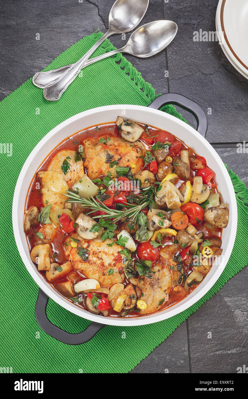 Spezzatino di pollo. Pollo in casseruola con un bicchiere di vino rosso, spezie e verdure, pronto a mangiare. Foto Stock