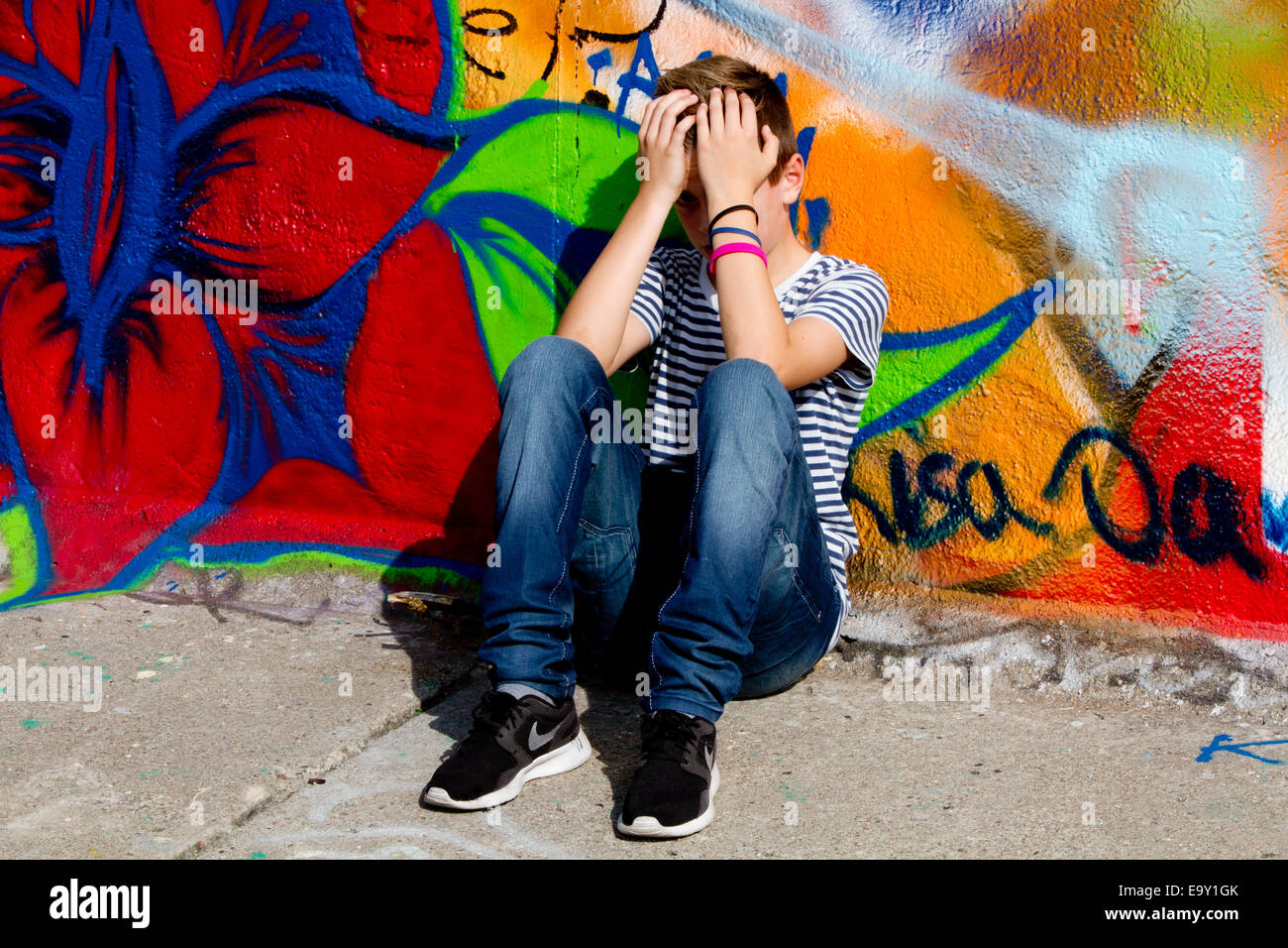 Muro di Berlino graffiti kid sat holding testa in mani Foto Stock