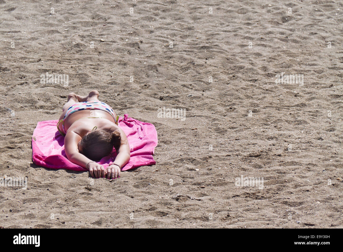 Una donna si trova su una spiaggia di sabbia di abbronzarvi al sole. Foto Stock