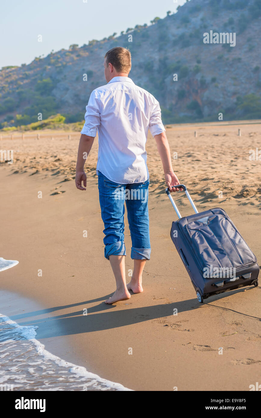 Uomo con una valigia a piedi lungo la spiaggia Foto Stock