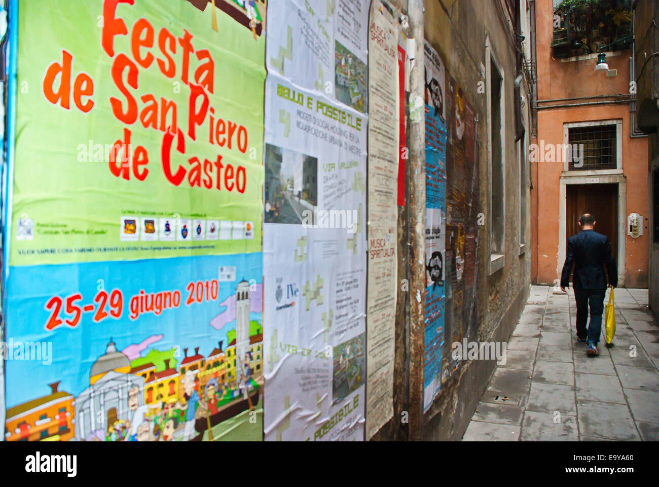 Uomo che cammina vicoletto coperto con manifesti pubblicitari a Venezia, Italia. Foto Stock