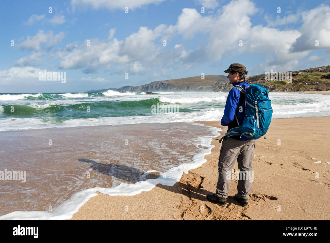 Walker guardando le onde che si infrangono in a Sandwood Bay, Sutherland Scotland Regno Unito Foto Stock