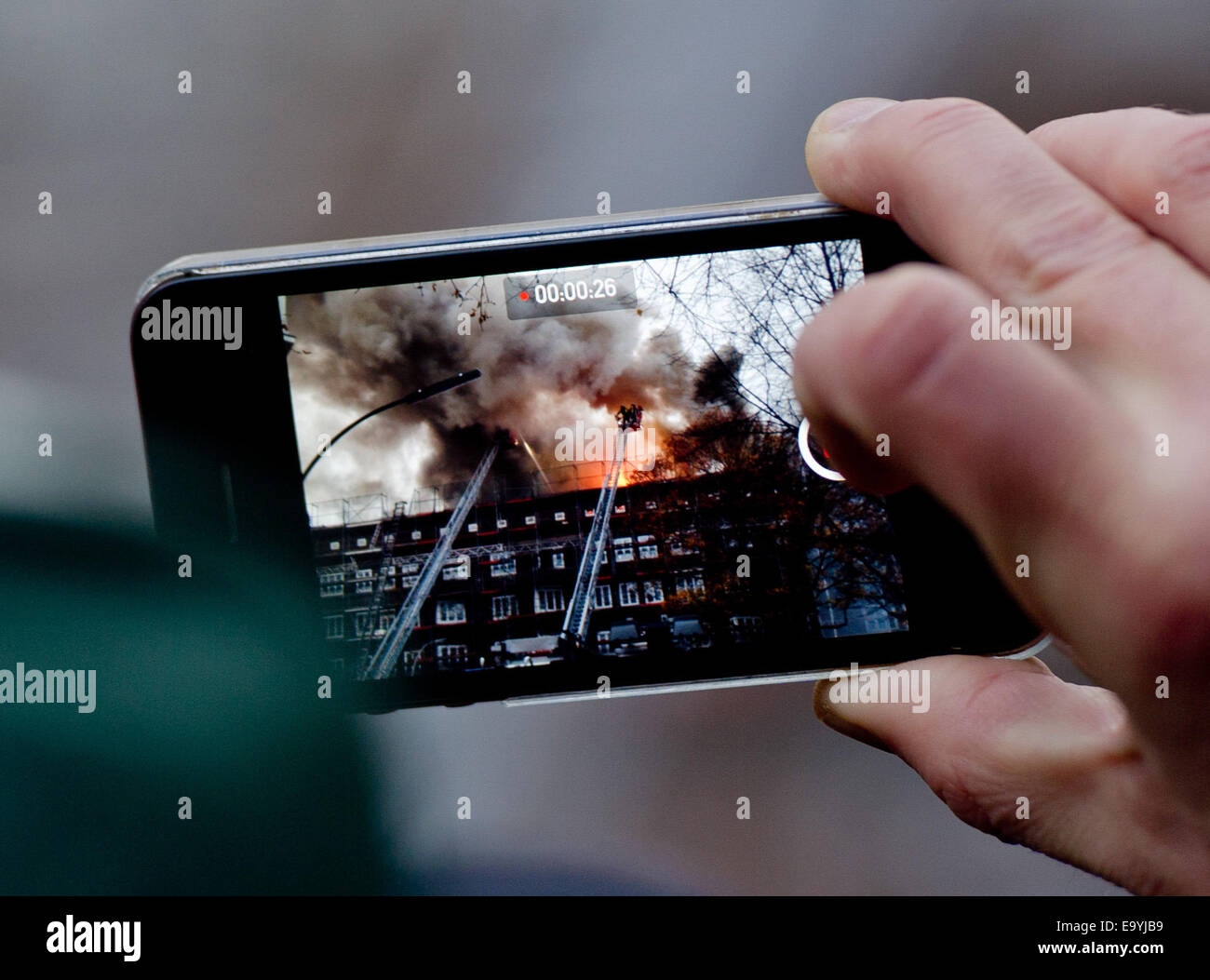 Amburgo, Germania. 04 Nov, 2014. Un uomo film un incendio sul tetto di una casa con il suo smartphone ad Amburgo, Germania, 04 novembre 2014. Una vasta operazione di mettere fuori fuoco nel distretto di Eimsbuettel. Credito: dpa picture alliance/Alamy Live News Foto Stock