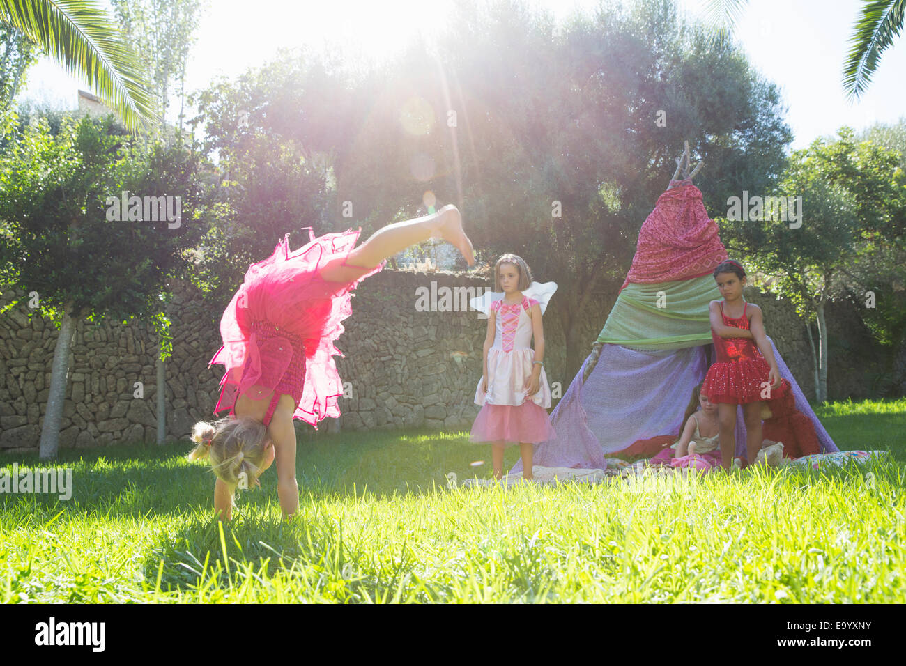 Girls Watching amico in costume fata facendo handstand in giardino Foto Stock