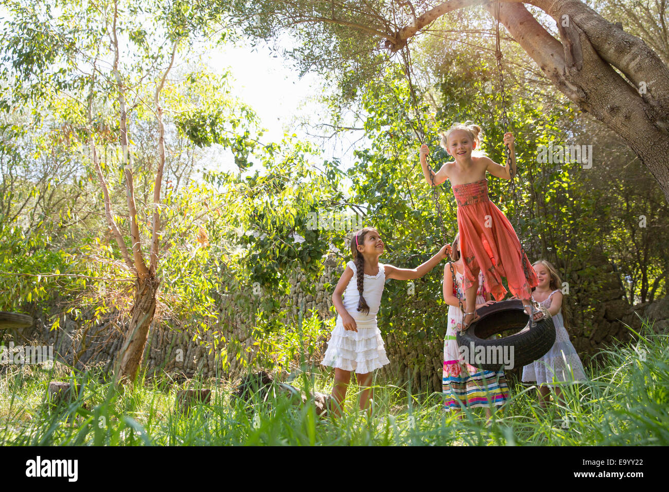 Le quattro ragazze giocando su albero di rotazione dei pneumatici in giardino Foto Stock