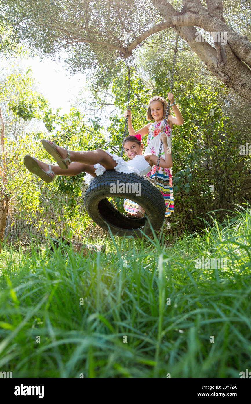 Due ragazze seduti e in piedi su albero oscillante nel giardino Foto Stock