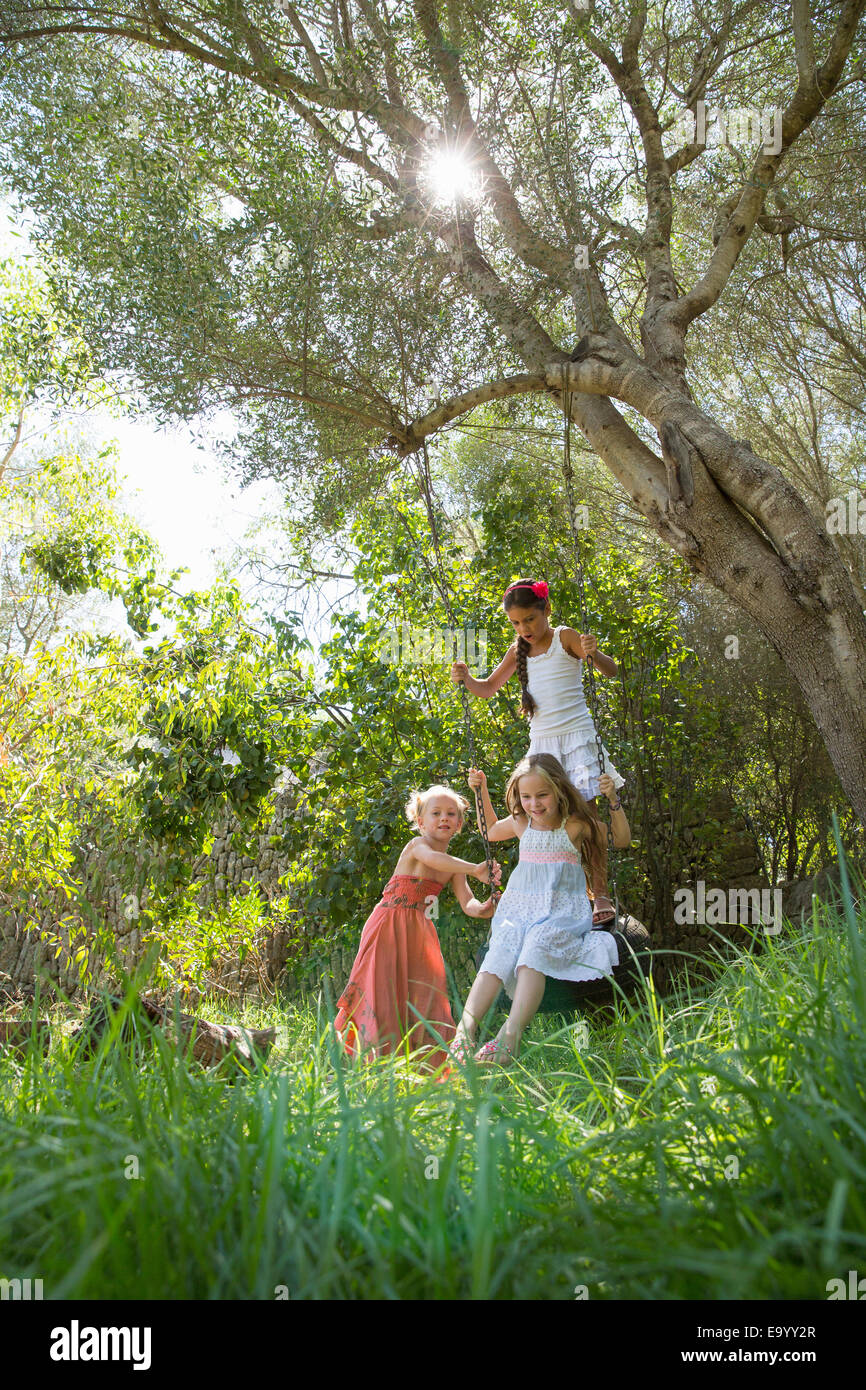 Le tre ragazze giocando su albero di rotazione dei pneumatici in giardino Foto Stock