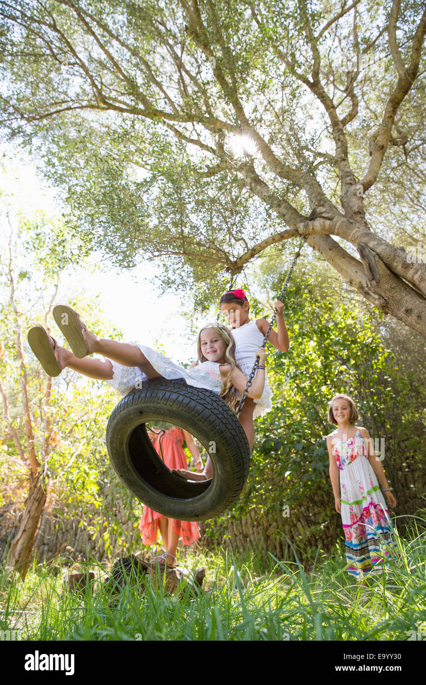 Basso angolo vista di quattro ragazze giocando su albero di rotazione dei pneumatici in giardino Foto Stock
