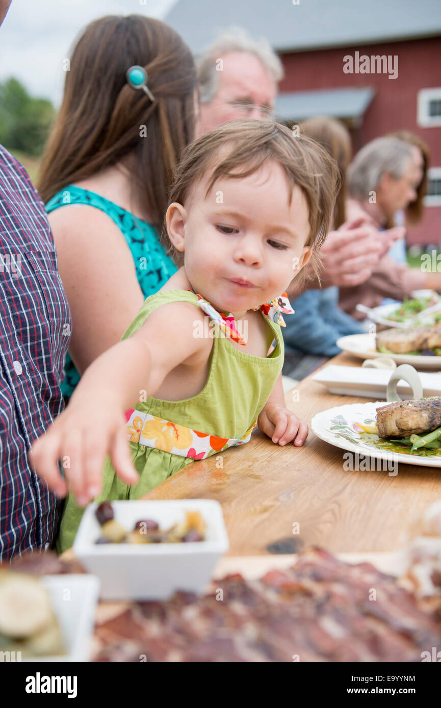 Un giovane bambino raccolta olive dal piatto al pasto familiare, all'aperto Foto Stock