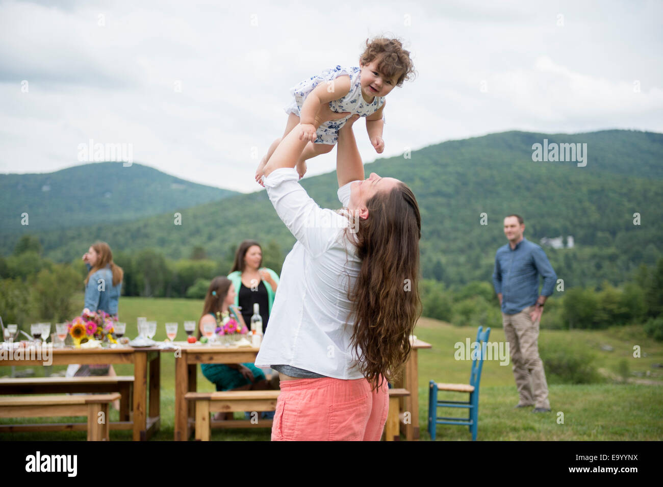 Metà donna adulta holding Baby girl in aria alla riunione di famiglia, all'aperto Foto Stock