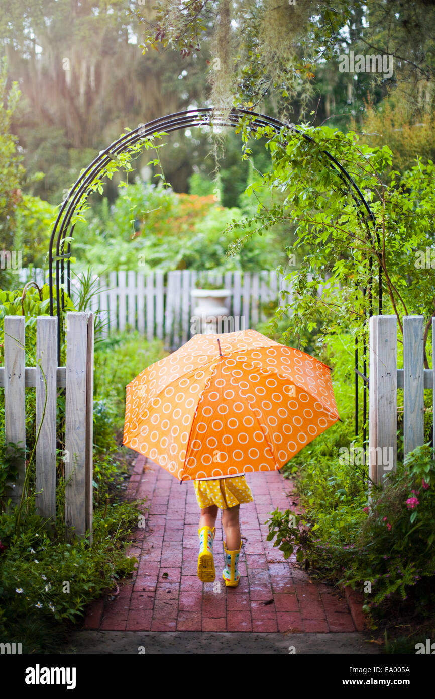 Ragazza camminare attraverso il cancello del giardino ombrello portante Foto Stock