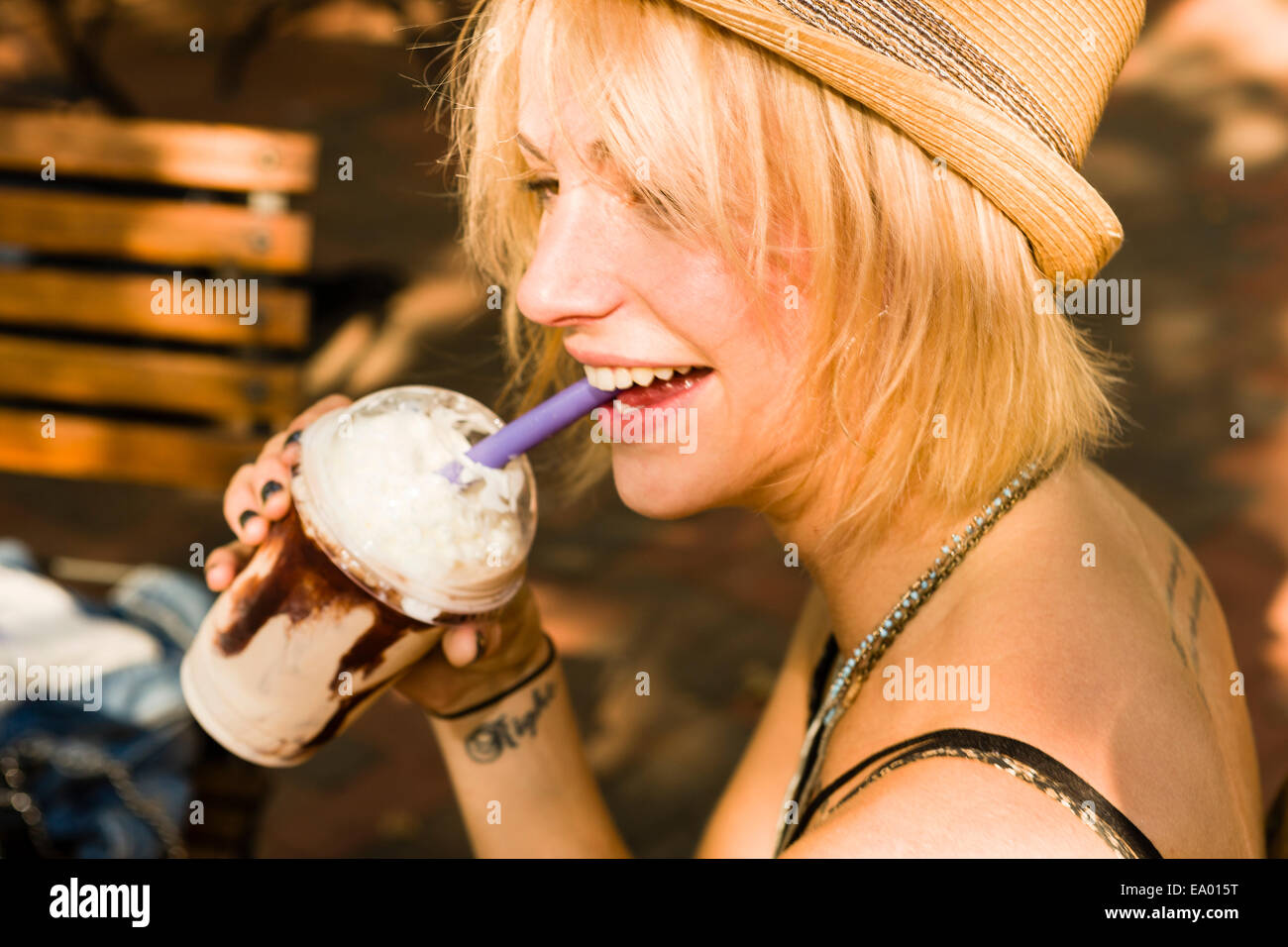 Giovane donna bere frappe con una paglia in posizione di parcheggio Foto Stock