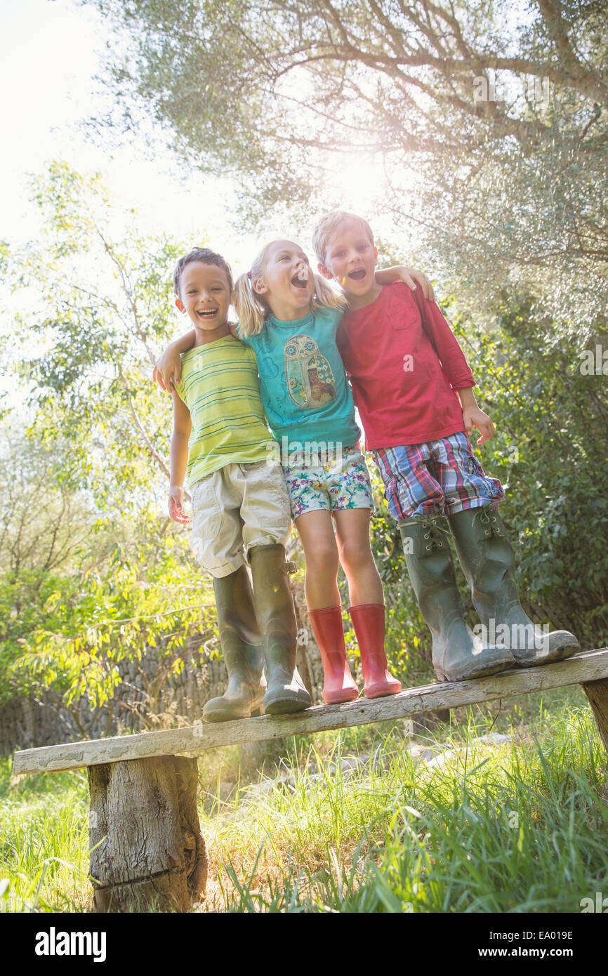 Tre bambini in piedi sul sedile del giardino con le braccia intorno a ciascun altro Foto Stock