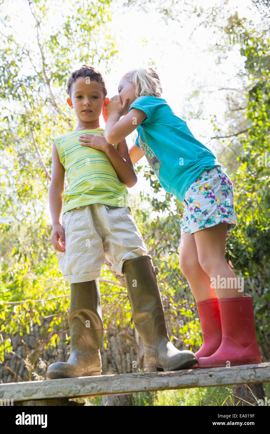 Ragazza whispering al ragazzo mentre in piedi sulla panchina da giardino Foto Stock