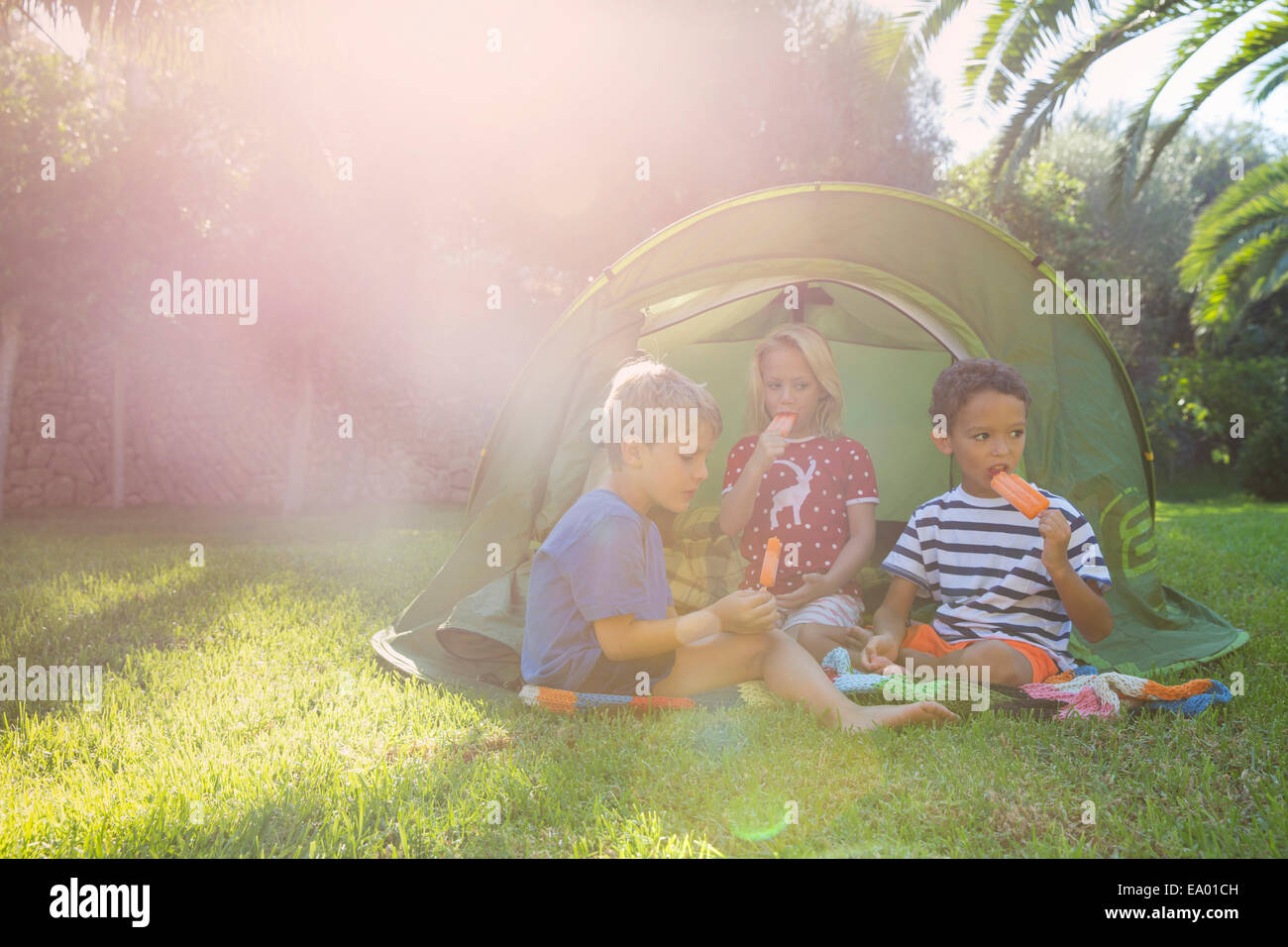 Tre bambini mangiare ghiaccioli in tenda da giardino Foto Stock