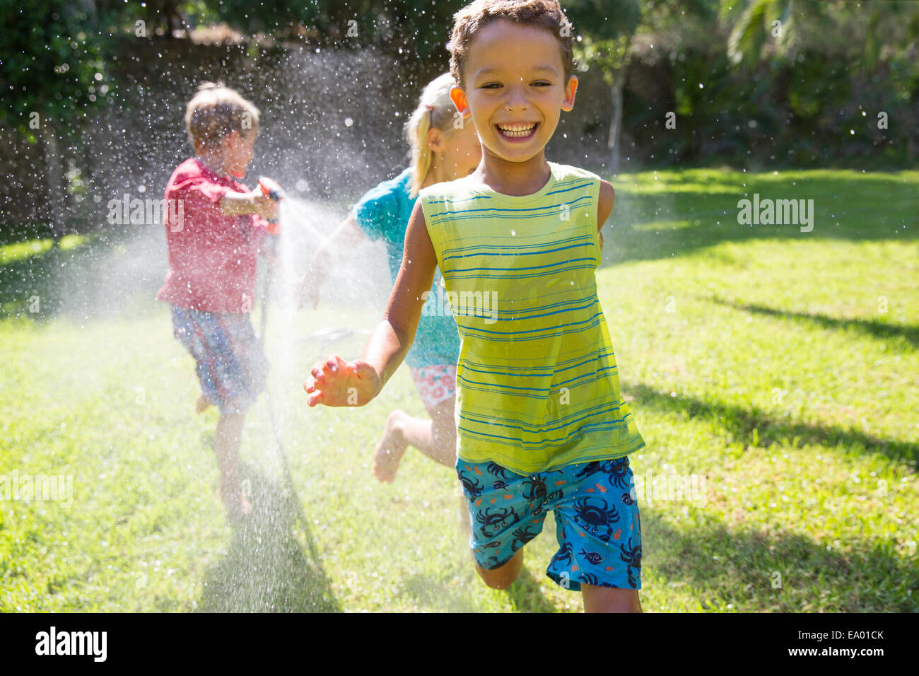 Tre bambini che si rincorrono in giardino con sprinkler acqua Foto Stock