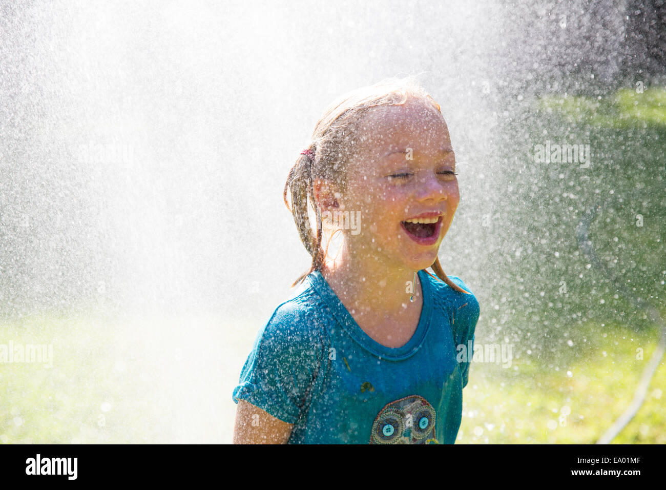 Girl getting schizzato da sprinkler acqua in giardino Foto Stock