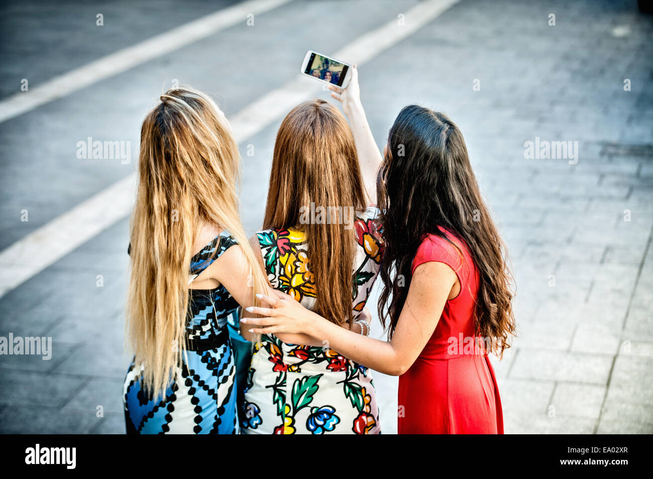 Vista posteriore di tre giovani donne tenendo selfie con lo smartphone, Cagliari, Sardegna, Italia Foto Stock