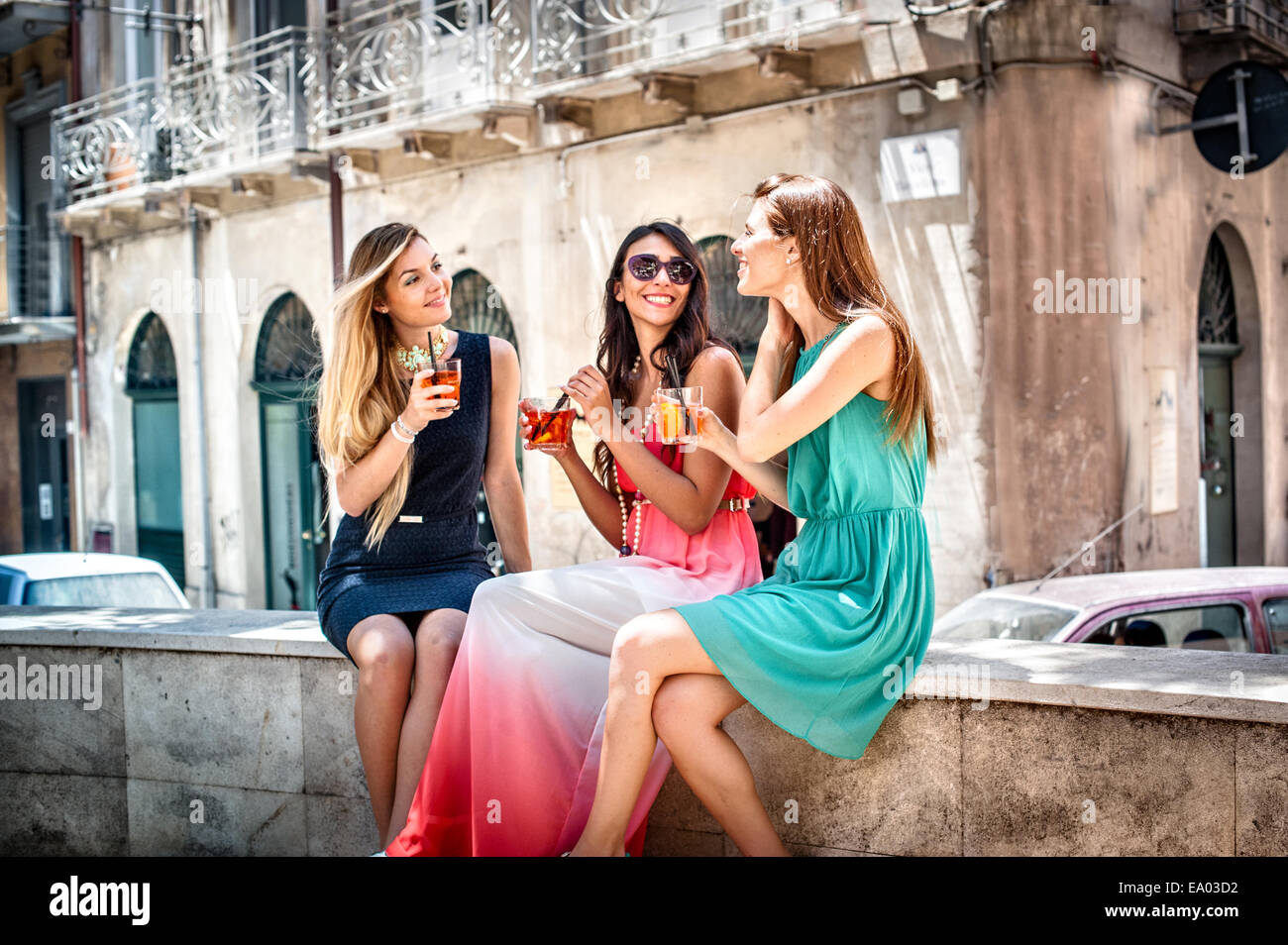 Tre giovani alla moda amici femmina avente il cocktail di cafè sul marciapiede parete, Cagliari, Sardegna, Italia Foto Stock