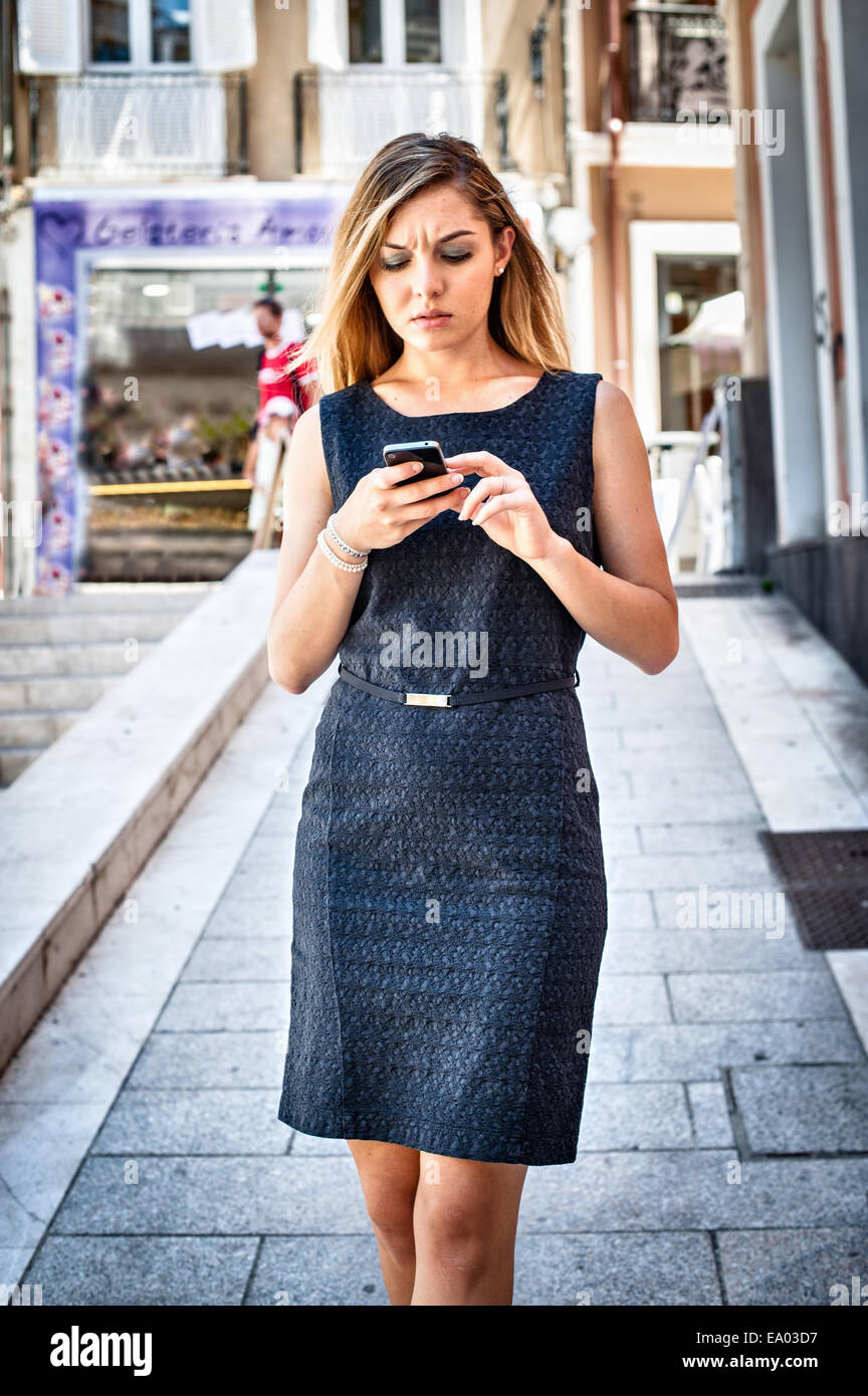 Impazienti giovane donna scrivere messaggi su smartphone su una strada di città Foto Stock